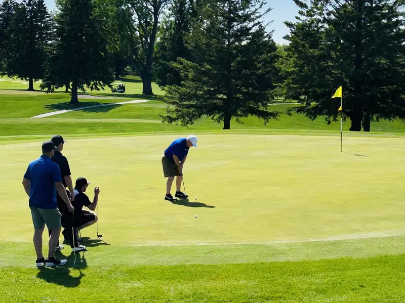 Golfer putting while teammates watch